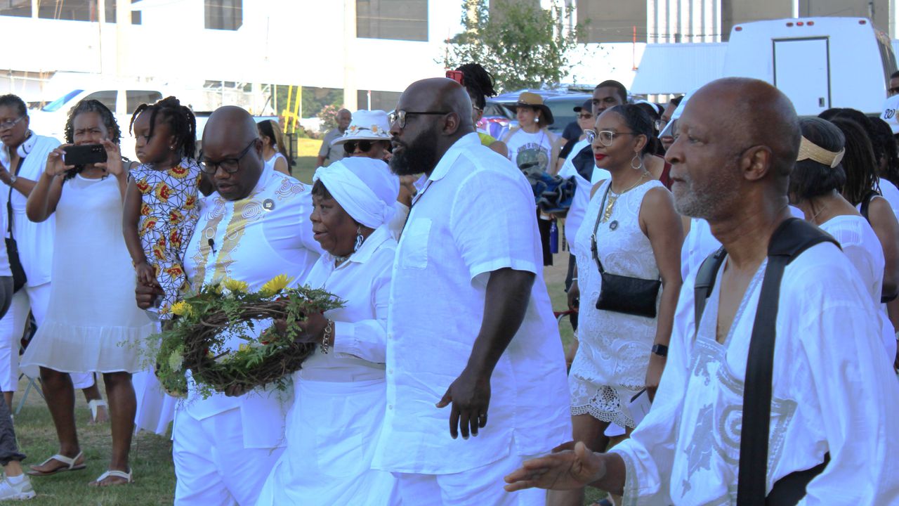 Clotilda descendant Lorna Gail Woods, with wreath, is assisted by Clotilda Descendants Association President Jeremy Ellis, to her left, and Shedrick Lefon Perry, to her right, during the association's Landing ceremony on July 8, 2023.