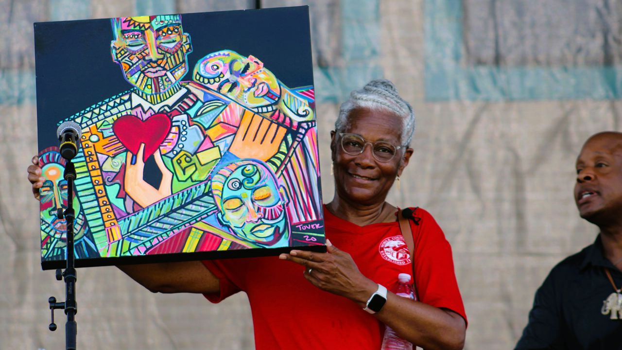 Mobile County Commissioner Merceria Ludgood holds up a painting presented by artists Ty Tover, right, during a community day of festivities celebrating the opening of the Africatown Heritage House on July 8, 2023.