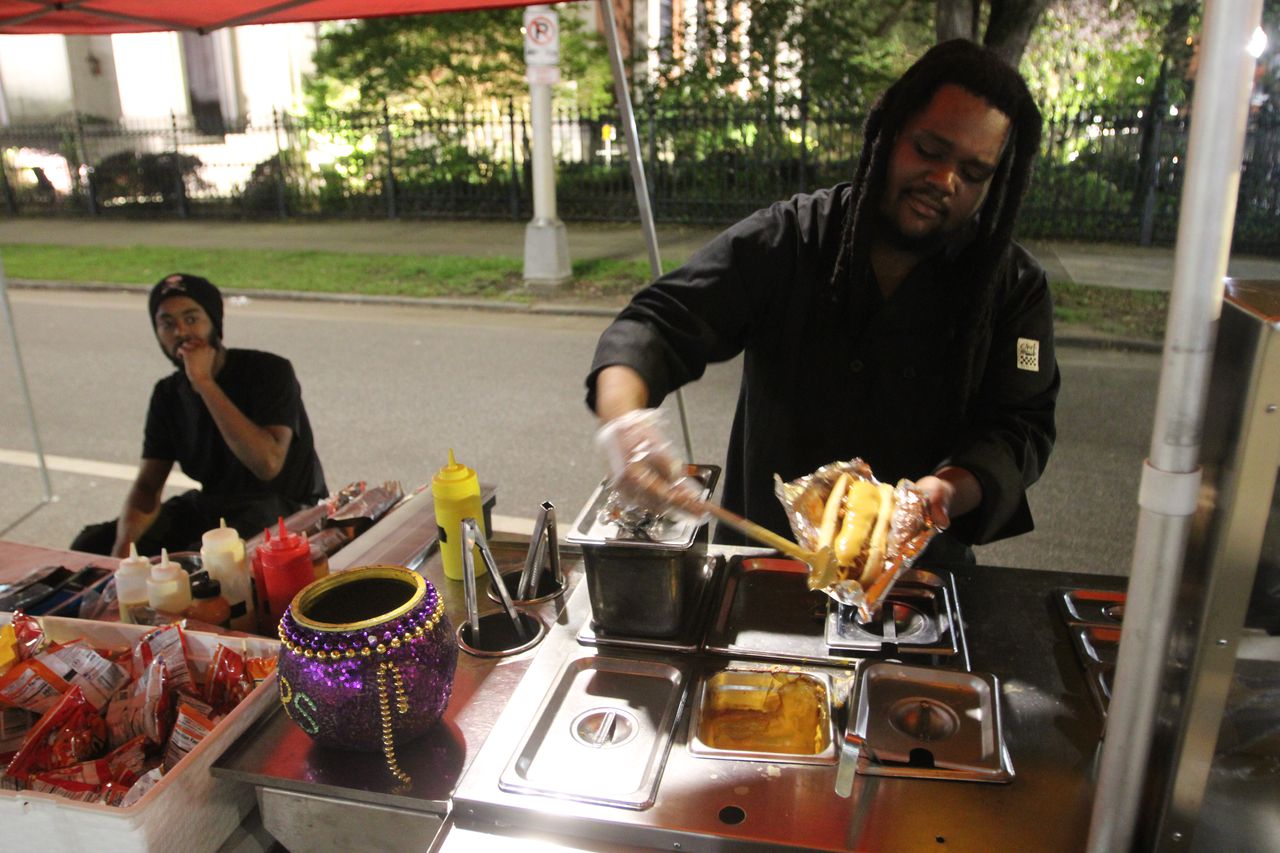 With the pillars of Mobile's cathedral in the background, Nazear Williams loads up a Frito pie dog at King Dogs on Cathedral Square.